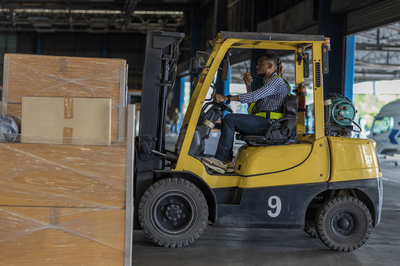 A forklift driver entering a warehouse with a loaded forklift.