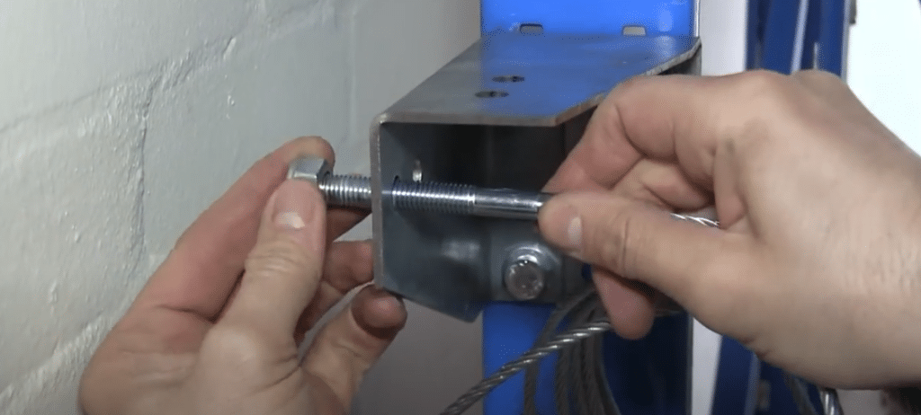 Man attaching cable to the first main bracket by passing the stud end through the outer vertical hole, and securing it with the supplied locking nut.