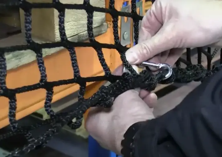 A close-up of someone looping a carabiner clip through netting to shorten the length of it.