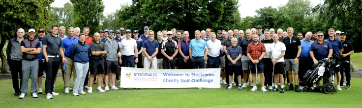 Official image for Stockdales Golf Day showing players on the golf course, with a Stockdales event banner in front of the group.